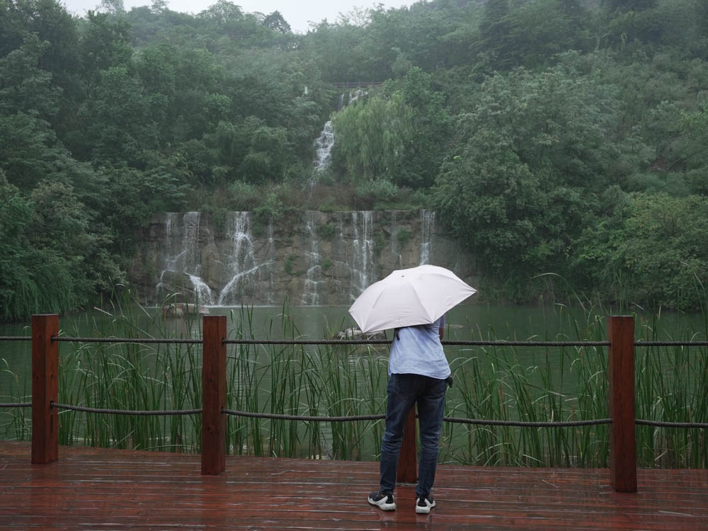 Jinlong Lake Dangkou Park includes glass trestle bridge, small canyon visitors enjoy the waterfall with umbrellas on rainy days
